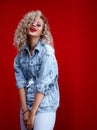 Young attractive stylish smiling woman having fun.curly girl dressed in a denim jacket and jeans on a red background Royalty Free Stock Photo