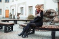 Young attractive stylish woman in trendy winter coat in black gloves with a woolen scarf in black shoes with heels sitting Royalty Free Stock Photo