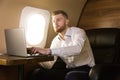 Young attractive and successful businessman working while sitting in the chair of his private business plane