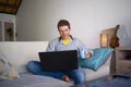 Young attractive and successful man working from home living room sitting on couch networking on laptop computer drinking coffee h Royalty Free Stock Photo