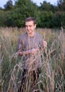 A young attractive thin guy standing in the tall grass on the forest background.