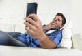 Young attractive tired and overworked falling asleep yawning at home couch with mobile phone and digital tablet Royalty Free Stock Photo