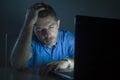 Young attractive and tired unshaven man working late night on laptop computer in the dark feeling frustrated and exhausted in