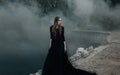 Young attractive Witch walking on the bridge in heavy black smoke. Royalty Free Stock Photo