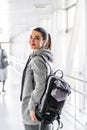 Young attractive woman with backpack next to big window in airport.