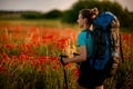 Young attractive woman with backpack and walking sticks stands on field of poppies Royalty Free Stock Photo