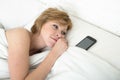 Young attractive woman in bed alone with mobile phone as sleeping partner in internet and smart phone addiction concept Royalty Free Stock Photo