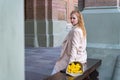 Young attractive woman in beige coat sits on bench with bouquet of tulips looking over her shoulder at the camera Royalty Free Stock Photo