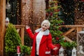 Woman posing under the snowing on the wooden terrace with Christmas background.