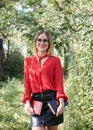 Young attractive woman with blond short hair, wearing red shirt and black skirt, holding books in her hands. Three-quarter Royalty Free Stock Photo