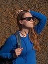 Young attractive woman in blue hoody black sunglasses on wall background listening to music with Wi-Fi headphones