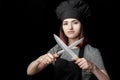 Young attractive woman chef in black uniform holds Two knives on black background. Focus on knives Royalty Free Stock Photo