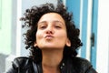 Young attractive woman with curly hair gesturing for a camera selfie and sending kisses. Urban city people concept