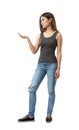 Young attractive woman in gray sleeveless top and blue jeans standing in half-turn with right arm bent at elbow and