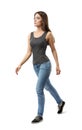 Young attractive woman in gray sleeveless top and blue jeans walking in half-turn and looking aside isolated on white