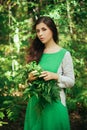 A young, attractive woman in a green dress from a medieval villager holds a fern leaf in her hands. A village herbalist collects h