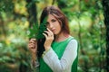 A young, attractive woman in a green dress from a medieval villager holds a fern leaf in her hands. A village herbalist collects h