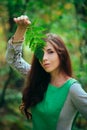 A young, attractive woman in a green dress from a medieval villager holds a fern leaf in her hands. A village herbalist collects h