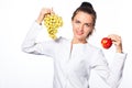 young attractive woman, holding a grape in one hand and a red apple in the other, looking joyful and happy, standing Royalty Free Stock Photo