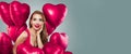 Young attractive woman holding vivid pink heart balloons on gray background