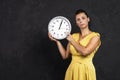 A young attractive woman holds a round clock in her hands. The concept of time. The girl watches the time