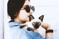 Young attractive woman hugging pussy cat in hands. Cute and glamorous girl in trendy sunglasses posing with her Siamese cat Royalty Free Stock Photo