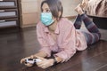 Young attractive woman in hygienic mask plays computer game, laying on the floor of her room. Isolation time spending, leisure on