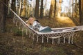 Young attractive woman laying in the hammock in sunny forest, resting after active hike - photo with selective focus