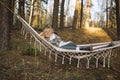 Young attractive woman laying in the hammock in sunny forest, resting after active hike - photo with selective focus