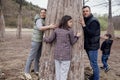 Young attractive woman, man and pretty teenage girl are hugging large cypress trunk