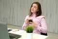 Young attractive woman at a modern office desk with coffee in hands, working with laptop, looking away, thinking about something Royalty Free Stock Photo