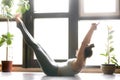 Young attractive woman in Paripurna Navasana pose, home interior