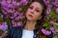 Young attractive woman in pink flowers in the garden. Girl with curly hair in white dress and black leather jacket outdoor Royalty Free Stock Photo