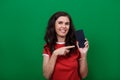 Young attractive woman is pointing on blank screen of phone in her hand and looks into a camera Royalty Free Stock Photo