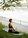 Back of a young attractive woman practicing yoga, sitting in Lotus pose, wearing in sportswear in the park Royalty Free Stock Photo