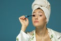 Young attractive woman putting eye mascara over blue background Royalty Free Stock Photo
