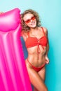 Young attractive woman in red bikini and sunglasses posing with pink inflatable mattress, isolated on green background Royalty Free Stock Photo