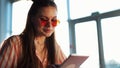 Young attractive woman in red sunglasses with tablet computer sitting in cafe. Beautiful girl in airport or shoppping