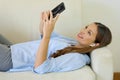 Young attractive woman relaxing on the couch at home choosing music on smart phone listening to music with wireless earphones Royalty Free Stock Photo