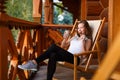Young attractive woman sitting outdoors on deck chair with coffee cup and oat cookie at mountain resort. Female on Royalty Free Stock Photo