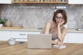 Young attractive woman sitting at the table and working on laptop in the kitchen at home Royalty Free Stock Photo