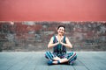 Young attractive woman sitting in yoga pose and smiling outdoor over red wall, image toned. Chinese girl amuses, summertime.