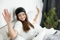 Young attractive woman with sleeping mask on her head sitting in bed in bright bedroom yawning in the morning Royalty Free Stock Photo