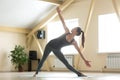 Young attractive woman standing in Utthita Trikonasana pose, hom