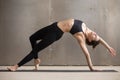 Young attractive woman stretching in Camatkarasana pose, grey st