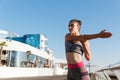 Young attractive woman stretching hands and warming-up before workout. Runner doing exercises on the seaside pier Royalty Free Stock Photo