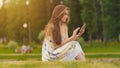 Young attractive woman in summer dress sits on green grass with mobile phone in hands. A park. Summer. Recreation. Royalty Free Stock Photo