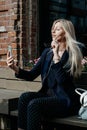 A young attractive woman takes a picture of herself on her smartphone, sitting on a street bench during the lunch break Royalty Free Stock Photo