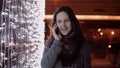 Young attractive woman talking on the phone in the falling snow at Christmas night standing near lights wall, Royalty Free Stock Photo