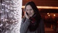 Young attractive woman talking on the phone in the falling snow at Christmas night standing near lights wall, Royalty Free Stock Photo